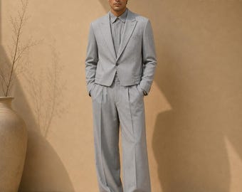 May include: A light gray suit consisting of a cropped blazer with a single button closure and matching wide-leg trousers with a center crease. The outfit is paired with a light gray button-down shirt. The text SuitCrafters appears in the corner.