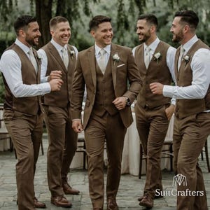 May include: Five men wearing brown suits, white shirts, and light-colored ties. The suits include a jacket, vest, and pants. The men are smiling and appear to be at an outdoor event. The logo "SuitCrafters" is visible in the bottom right corner.