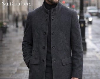 May include: A charcoal gray overcoat with a mandarin collar and button closure. The coat has two front pockets and is worn over a black turtleneck. The image includes the text "SuitCrafters" in the upper left corner.