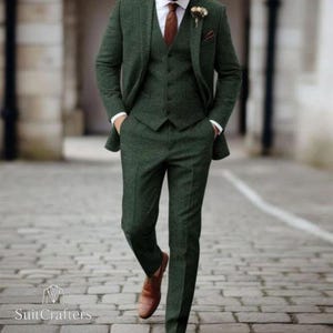Peut inclure: Un costume trois pièces en tweed vert, comprenant une veste, un gilet et un pantalon. Le costume est associé à une chemise blanche et une cravate marron. Des chaussures en cuir marron complètent l'ensemble. Le logo "SuitCrafters" est visible en bas.