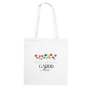May include: White tote bag with a colorful floral design and the text "GARDD Mam" in black. The flowers are in shades of orange, pink, blue, and yellow. The bag has two white handles.