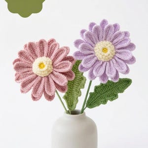 Op de afbeelding: Een witte vaas met twee gehaakte bloemen, een roze en een paarse, met gele centra. Groene bladeren en stelen begeleiden de bloemen. De afbeelding bevat de tekst "PDF PATTERN".