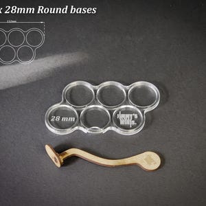 May include: A clear acrylic base for six 28mm round bases, with the text "Jimmy's Minis" etched on it. A wooden tool is also included. The text "For 6 x 28mm Round bases" is at the top.