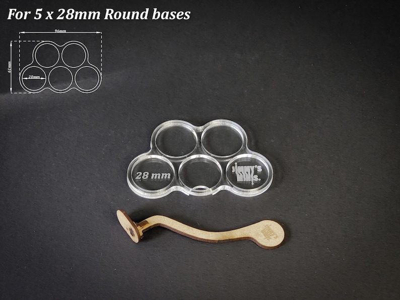 Puede incluir: Base de acr&iacute;lico transparente para 5 bases redondas de 28 mm, con un mango de madera. La base tiene cinco recortes circulares, cada uno de 28 mm de di&aacute;metro. El texto en la base dice "Jimmy's Minis". El mango de madera es curvo.