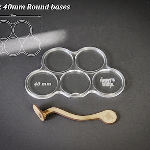 Puede incluir: Soporte de base acr&iacute;lico transparente para cinco bases redondas de 40 mm, con un mango de madera. El soporte tiene el texto "40 mm" y "Jimmy's Minis" grabado. La imagen tambi&eacute;n incluye un diagrama con medidas.