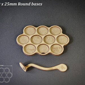 May include: A wooden tray with ten circular cutouts, each 2.5cm in diameter, and a matching handle. The tray is designed to hold round bases. The text "For 10 x 25mm Round bases" is at the top.