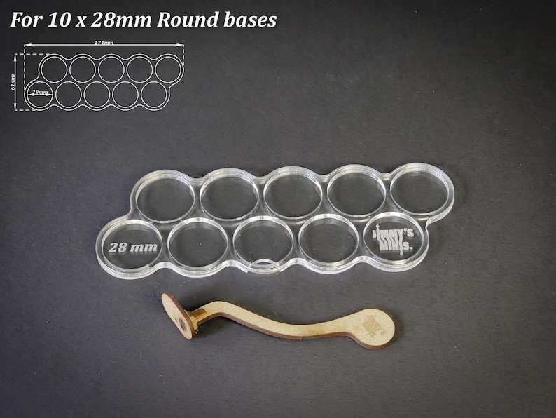 May include: Clear acrylic base holder for 10 miniature figures with 28 mm round bases. Includes a wooden tool for easy placement. The text "For 10 x 28mm Round bases" is at the top. The holder is 17.4cm long and 6.1cm wide.