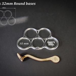 Puede incluir: Soporte de base acr&iacute;lico transparente para 5 bases redondas de 32 mm, con mango de madera. El soporte tiene cinco recortes circulares, cada uno etiquetado con "32 mm". El texto "For 5 x 32mm Round bases" est&aacute; en la parte superior.