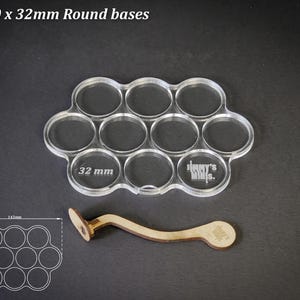 Op de afbeelding: Transparante acryl basis voor 10 ronde bases van 32 mm, met een houten handvat. De basis heeft 10 cirkelvormige uitsparingen, elk met een afmeting van 3,2 cm. De tekst "For 10 x 32mm Round bases" staat bovenaan.