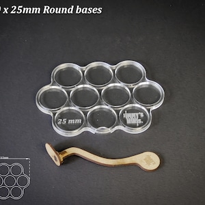 Op de afbeelding: Transparante acryl basis houder voor 10 ronde bases, elk met een diameter van 25 mm. Inclusief een houten handvat voor eenvoudige bediening. De tekst "For 10 x 25mm Round bases" staat bovenaan.