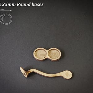 May include: Two wooden round bases, each 25mm in diameter, and a curved wooden handle. The bases are connected and have text that reads "25 mm". The handle has a small, circular design on one end. The text "For 2 x 25mm Round bases" is at the top.
