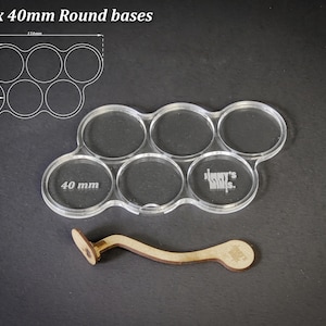 May include: Clear acrylic base holder for six 40mm round bases, with a wooden tool. The text "For 6 x 40mm Round bases" is at the top. The holder has the text "Jimmy's Minis" on it.