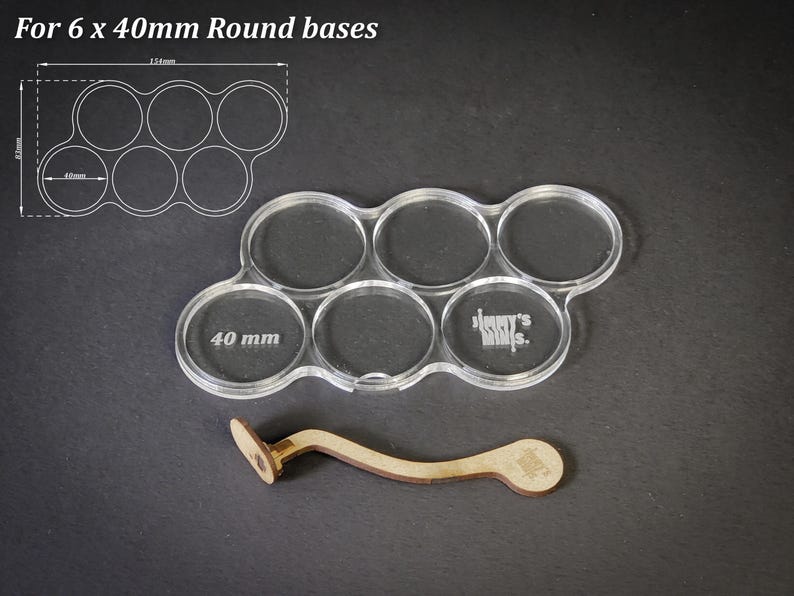 May include: Clear acrylic base holder for six 40mm round bases, with a wooden tool. The text "For 6 x 40mm Round bases" is at the top. The holder has the text "Jimmy's Minis" on it.