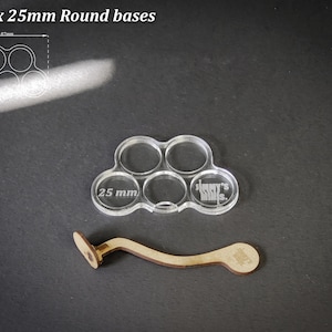 Puede incluir: Soporte de base acr&iacute;lico transparente para 5 bases redondas de 25 mm, con un mango de madera. El soporte tiene cinco aberturas circulares, cada una etiquetada con "25 mm". El mango de madera es curvo.