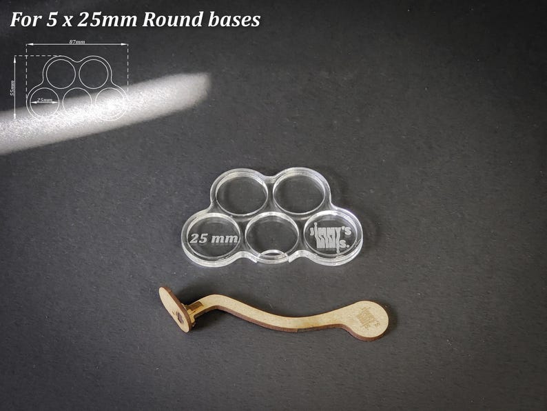 Puede incluir: Soporte de base acr&iacute;lico transparente para 5 bases redondas de 25 mm, con un mango de madera. El soporte tiene cinco aberturas circulares, cada una etiquetada con "25 mm". El mango de madera es curvo.