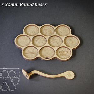 May include: A wooden tray with ten circular cutouts, labelled "32mm" and "Jimmy's Minis", and a matching handle. The tray is designed to hold round bases. The text "For 10 x 32mm Round bases" is at the top.