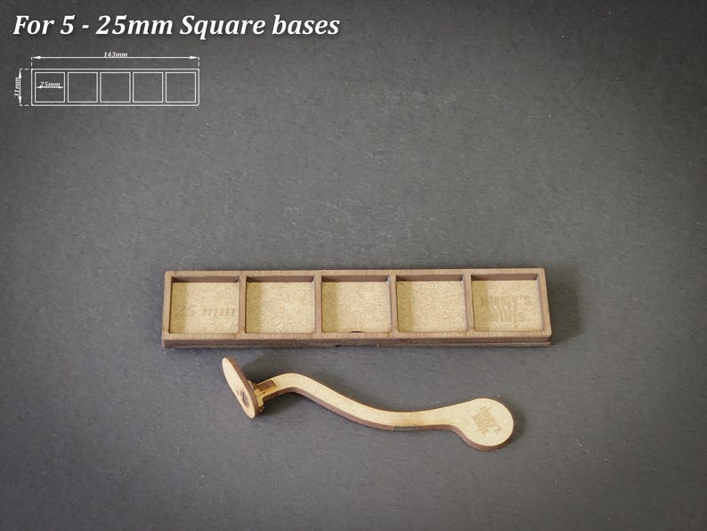 Puede incluir: Una base de madera para 5 bases cuadradas, cada una de 25 mm. La base es rectangular con cinco recortes cuadrados. Tambi&eacute;n se incluye un asa de madera curvada. El texto "For 5 - 25mm Square bases" est&aacute; en la parte superior.