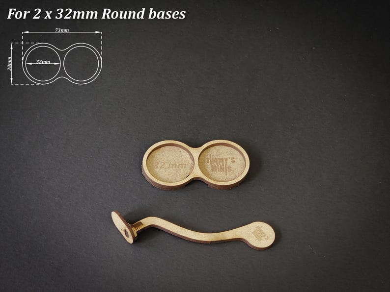 May include: Two wooden round bases, each 32mm in diameter, with a connecting handle. The bases are designed to hold miniatures. The text "For 2 x 32mm Round bases" is at the top. The text "Jimmy's Minis" is visible on one base.