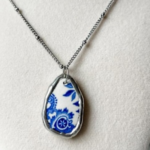 May include: A silver necklace with a pendant made from a piece of blue and white ceramic. The ceramic has a floral design. The text on the image says "#1 - beach found blue and white".