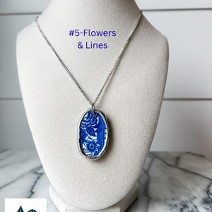 May include: Oval pendant necklace with a blue and white floral design set in a silver-tone metal frame. The necklace is displayed on a white mannequin. The text "#5-Flowers & Lines" is visible.