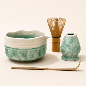 May include: A ceramic matcha bowl with a white upper rim and a turquoise crystalline glaze lower section, a bamboo whisk, a matching turquoise crystalline glazed whisk holder, and a long, thin, curved bamboo tea scoop for preparation.
