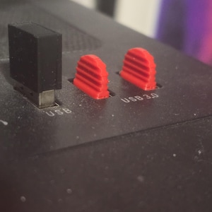 May include: A black electronic device panel featuring one black rectangular USB port cover and two red semi-circular USB 3.0 port covers with horizontal ridges. The text USB is printed near the black cover and USB 3.0 is printed near the red covers.