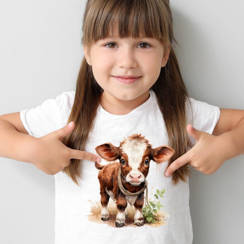 Puede incluir: Camiseta blanca con una ilustraci&oacute;n en acuarela de un ternero marr&oacute;n y blanco. El ternero tiene orejas grandes y una cuerda alrededor del cuello. El dise&ntilde;o incluye follaje verde y un trozo de hierba marr&oacute;n.