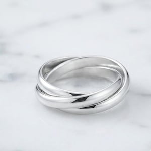 May include: A polished silver-toned ring featuring a triple-band interlocking design. The three smooth, rounded bands are connected to form a single cohesive piece, showcasing a reflective metallic surface with clean, continuous lines throughout.