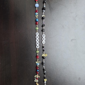 May include: Two beaded mask chains. One is multi-colored with the word "SUPER" spelled out in white letter beads. The other is black and gray with the word "BAT" spelled out in white letter beads. Both have gold and silver clasps.