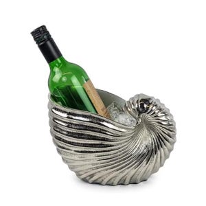 Op de afbeelding: Een zilverkleurige wijnkoeler in de vorm van een nautilus schelp houdt een groene wijnfles met een zwarte dop vast. De koeler is gevuld met ijsblokjes. Het ontwerp doet denken aan een zeeschelp.