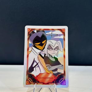May include: A trading card featuring two cartoon characters. One character is a tall, slender figure with a purple and black head and a white outfit. The other character has white hair and a black and green outfit. The card has the text "GUITARSPEAR".