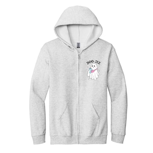 May include: A light gray zip-up hoodie featuring a graphic on the left chest of a white ghost wearing a pink crossbody bag and holding a blue drink. The text BOO-JEE is printed in black above the ghost, surrounded by small black star accents.