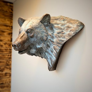 Può includere: Una scultura da parete raffigurante una testa di orso con finitura in bronzo metallizzato e accenti di patina scura. L'oggetto cattura la texture dettagliata del pelo, delle orecchie e dei tratti del muso dell'orso in una vista di profilo.
