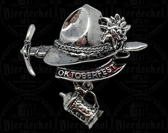 May include: A silver-toned Oktoberfest-themed pin featuring a traditional hat, pickaxe, and beer stein charm. The pin includes a banner with the word "OKTOBERFEST" in red lettering. The background is black with a repeating logo.