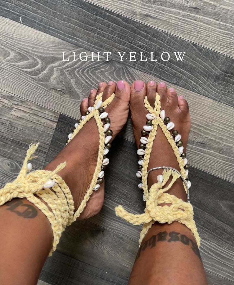 Puede incluir: Sandalias descalzas de ganchillo amarillo claro adornadas con conchas blancas y cuentas. Las sandalias se envuelven alrededor del tobillo y los dedos de los pies, creando un look playero y bohemio. El texto "LIGHT YELLOW" est&aacute; visible.
