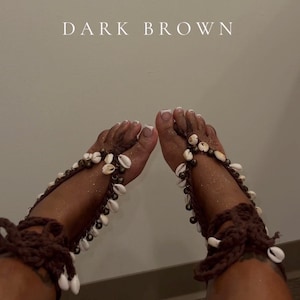Puede incluir: Joyas para pies de color marr&oacute;n oscuro con conchas blancas y detalles de ganchillo marr&oacute;n oscuro. El texto "DARK BROWN" se muestra en la parte superior de la imagen. Las joyas envuelven el pie y el tobillo.