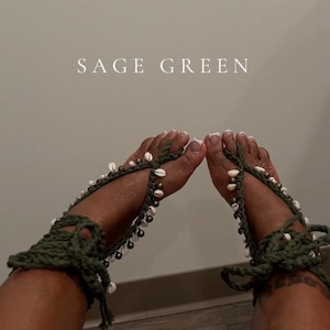 Puede incluir: Sandalias descalzas de ganchillo verde salvia adornadas con conchas blancas y peque&ntilde;as cuentas de bronce. Las sandalias se envuelven alrededor del tobillo y los dedos de los pies, con el texto "SAGE GREEN" en el fondo.