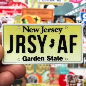 May include: A yellow and white New Jersey license plate sticker with the text "JRSY AF" and "Garden State".