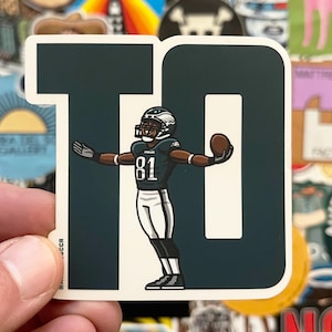 May include: A sticker depicting an American football player in an Eagles uniform, number 81, with arms outstretched, holding a football. The sticker is in the shape of the letters "T" and "O" in dark green. The background is a collage of other stickers.