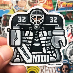 Può includere: Un'illustrazione in bianco e nero di un portiere di hockey che indossa una divisa bianca e nera con il numero 32 sul davanti. Il portiere tiene un bastone da hockey con la scritta "Warrior" su di esso. Il portiere indossa un casco nero con una maschera bianca e la scritta "Quick" su di essa.
