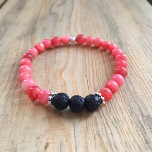 May include: A pink and coral beaded bracelet with three black lava rock beads and silver accents.