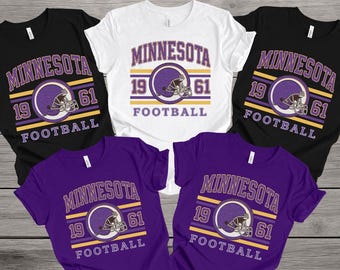 May include: Five t-shirts in black, white, and purple, each featuring a vintage design. The design includes the word "MINNESOTA", the numbers "19" and "61", a football helmet, and the word "FOOTBALL" in a retro style.