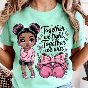 May include: A light green t-shirt featuring a cartoon girl with pink hair buns, wearing a pink sweater and black shorts. The shirt has the text "Together we fight, Together we win" with pink boxing gloves and a pink ribbon.