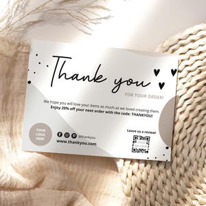 Peut inclure: Carte de remerciement blanche avec texte noir et design minimaliste. La carte comprend les mots "Thank you" dans une police manuscrite, ainsi qu'un code de réduction et des icônes de médias sociaux. La carte est sur un fond neutre.