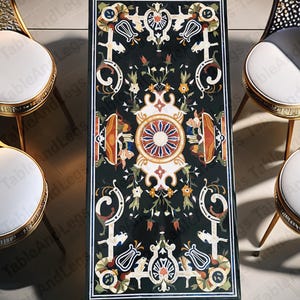 May include: A rectangular black marble table with intricate floral and geometric inlay designs in shades of white, orange, and yellow. The table is supported by a gold-colored base. The table is surrounded by gold-framed chairs with white seats.