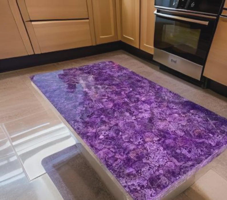 Puede incluir: Una encimera de cocina rectangular con una vibrante superficie p&uacute;rpura texturizada. La encimera se encuentra sobre un fondo de armarios de madera de color claro y un horno de acero inoxidable.