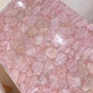 May include: A rectangular surface composed of irregularly shaped, light pink rose quartz pieces. The quartz pieces are set closely together, creating a mosaic-like pattern. The overall effect is a soft, textured, and naturally colored surface.