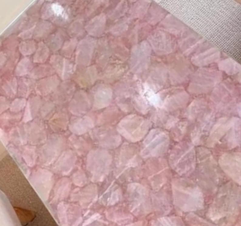 May include: A rectangular surface composed of irregularly shaped, light pink rose quartz pieces. The quartz pieces are set closely together, creating a mosaic-like pattern. The overall effect is a soft, textured, and naturally colored surface.