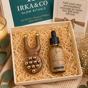 Puede incluir: Una caja de regalo de spa con un masajeador facial de madera y una botella de aceite de infusión de manzanilla. El masajeador es marrón con bolas de masaje doradas. La botella de aceite tiene un cuentagotas y la etiqueta dice "IRKA & CO GLOW RITUALS".