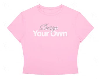 Może przedstawiać: Jasnoróżowy krótki top z krótkim rękawem z nadrukowanym z przodu napisem "Design Your Own". Słowo "Design" jest napisane kursywą, a "Your Own" pogrubioną, białą czcionką bezszeryfową, umieszczoną centralnie na klatce piersiowej.